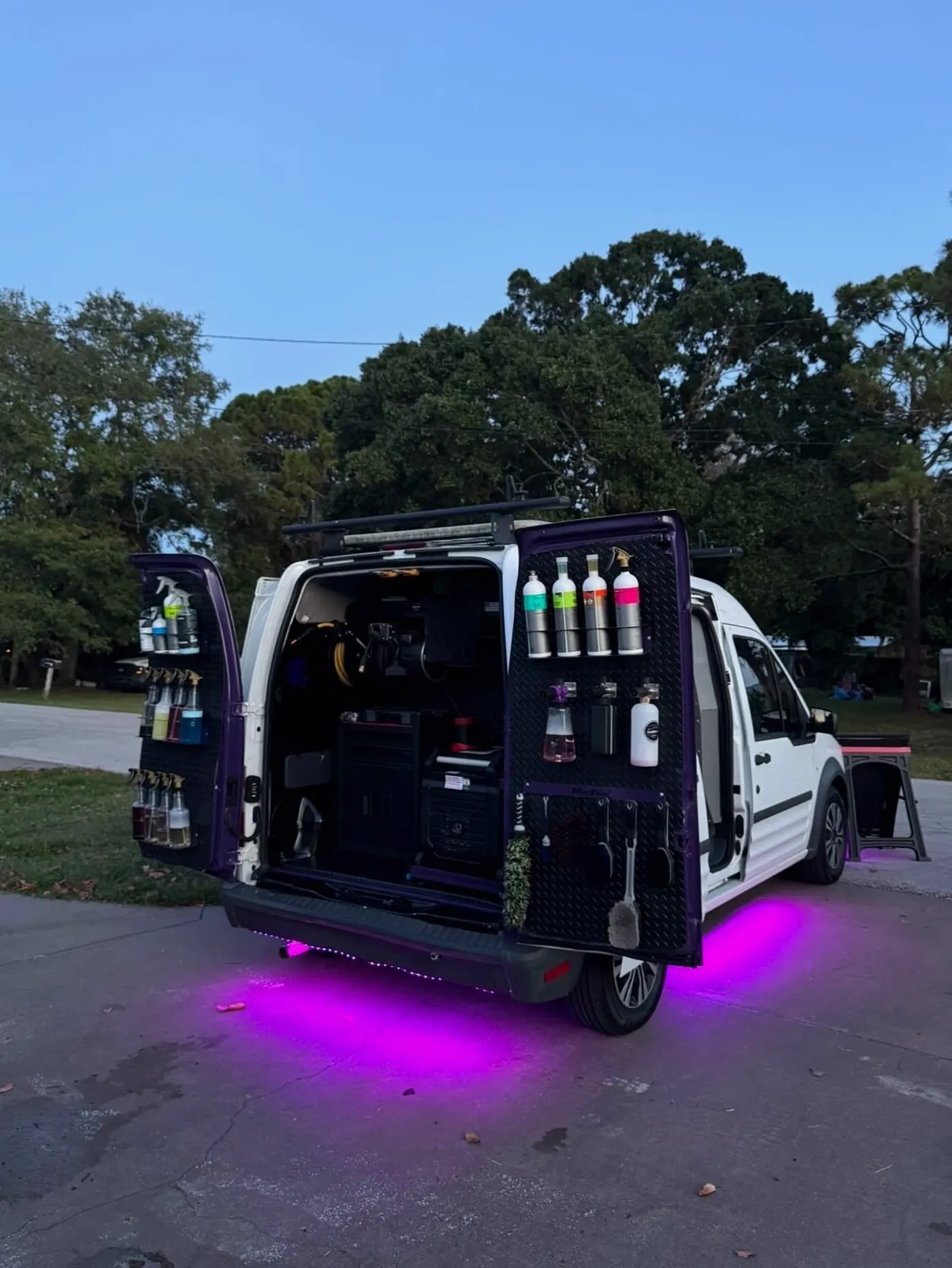 The GaliGloss detailing van with its doors open, fully stocked and glowing purple at dusk